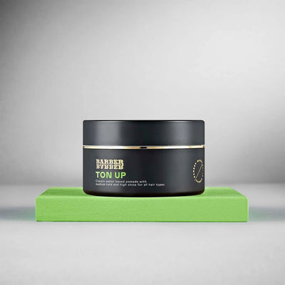 BARBER BARBER Ton Up Water-Based Pomade 100g - zwart potje op groen blok, grijze studio