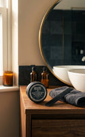 Reuzel Matte Styling Paste - potje bij kaars en kam op wastafelblad met spiegel