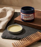 Blue Magic Pressing Oil - åben krukke på skifer med trækam, den gule olie synlig